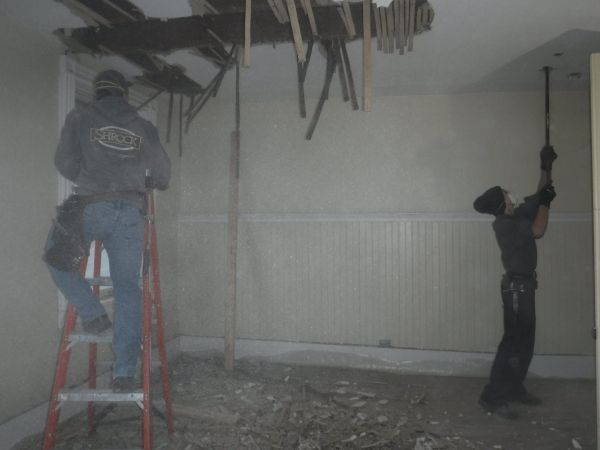 Two men are working on a ceiling in a room.