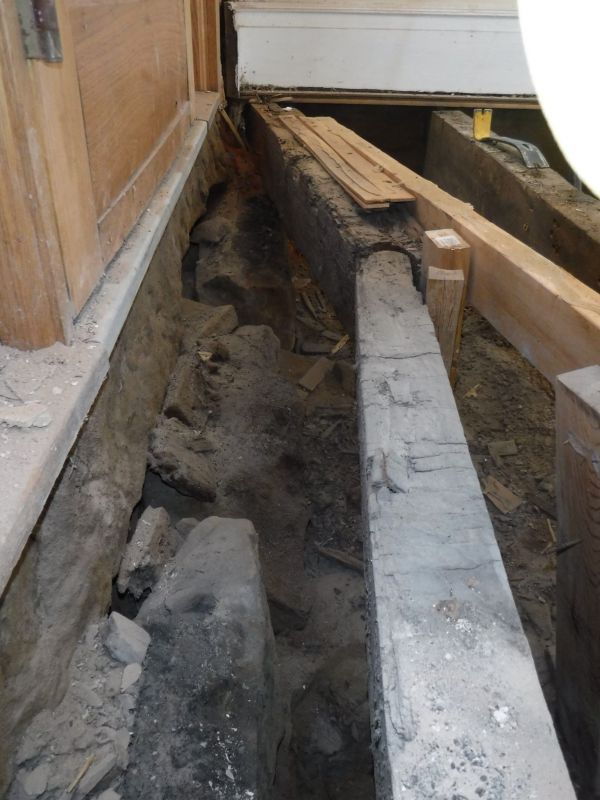 A concrete beam is laying in the dirt next to a wooden beam.