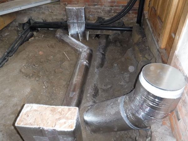 A metal pipe is sitting on the ground next to a brick wall.