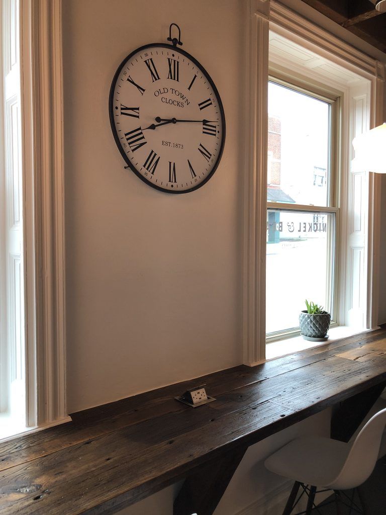 A large clock is hanging on a wall next to a window.