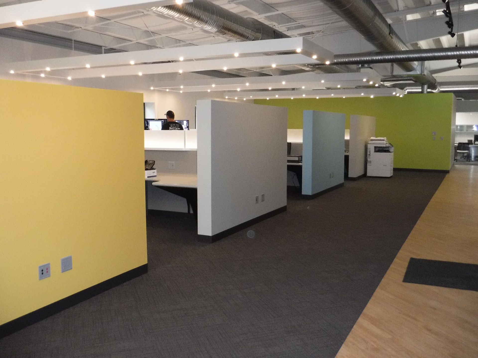 A row of cubicles in an office with yellow and blue walls.
