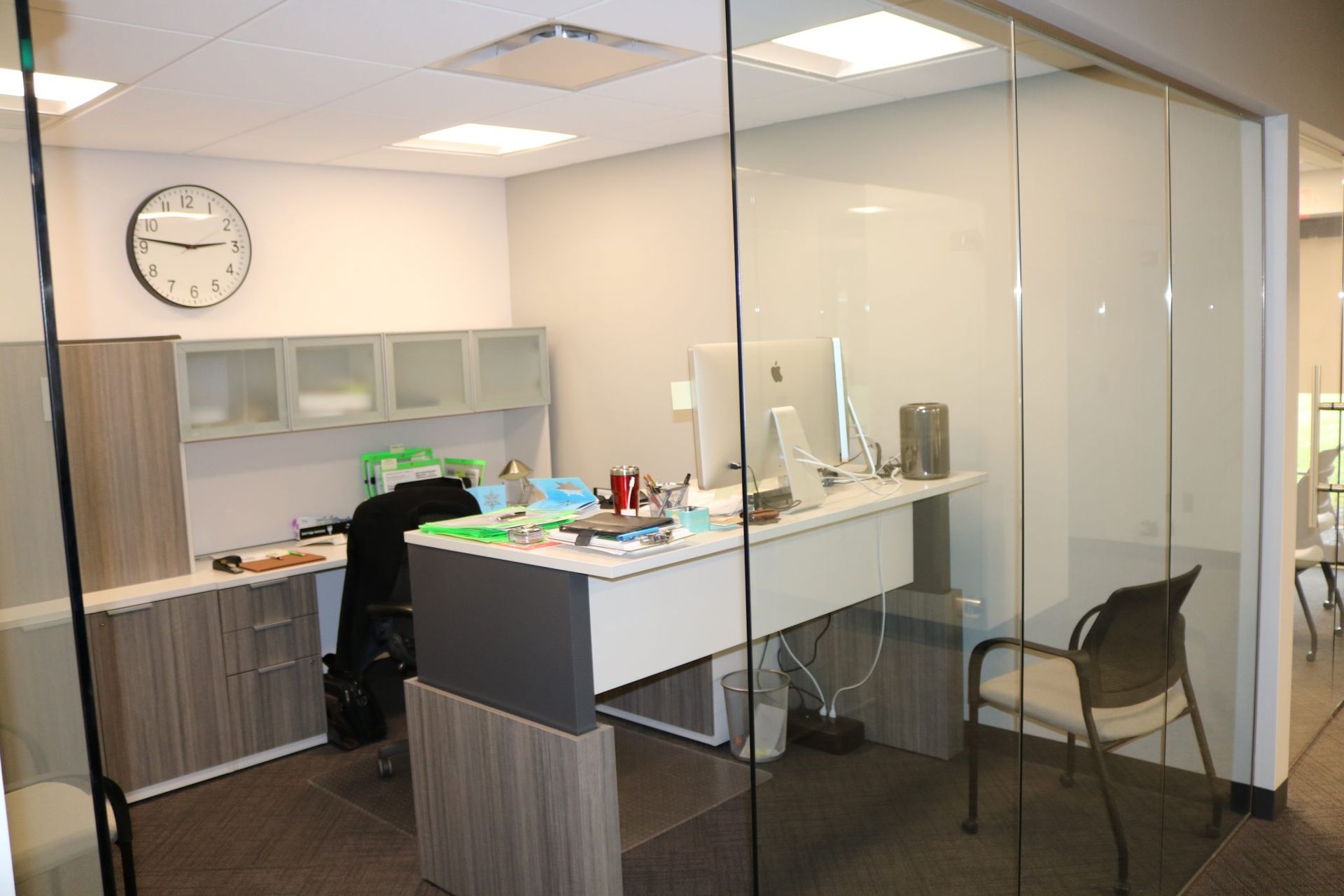 There is a clock on the wall above the desk in the office.