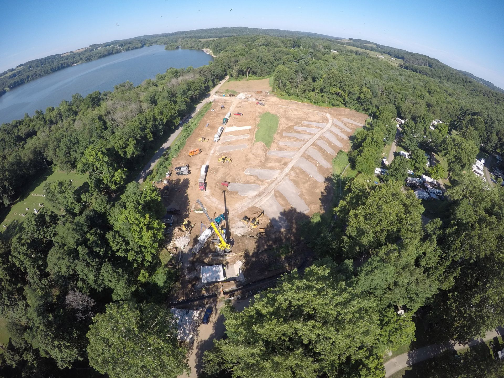 An aerial view of a construction site surrounded by trees and a lake.