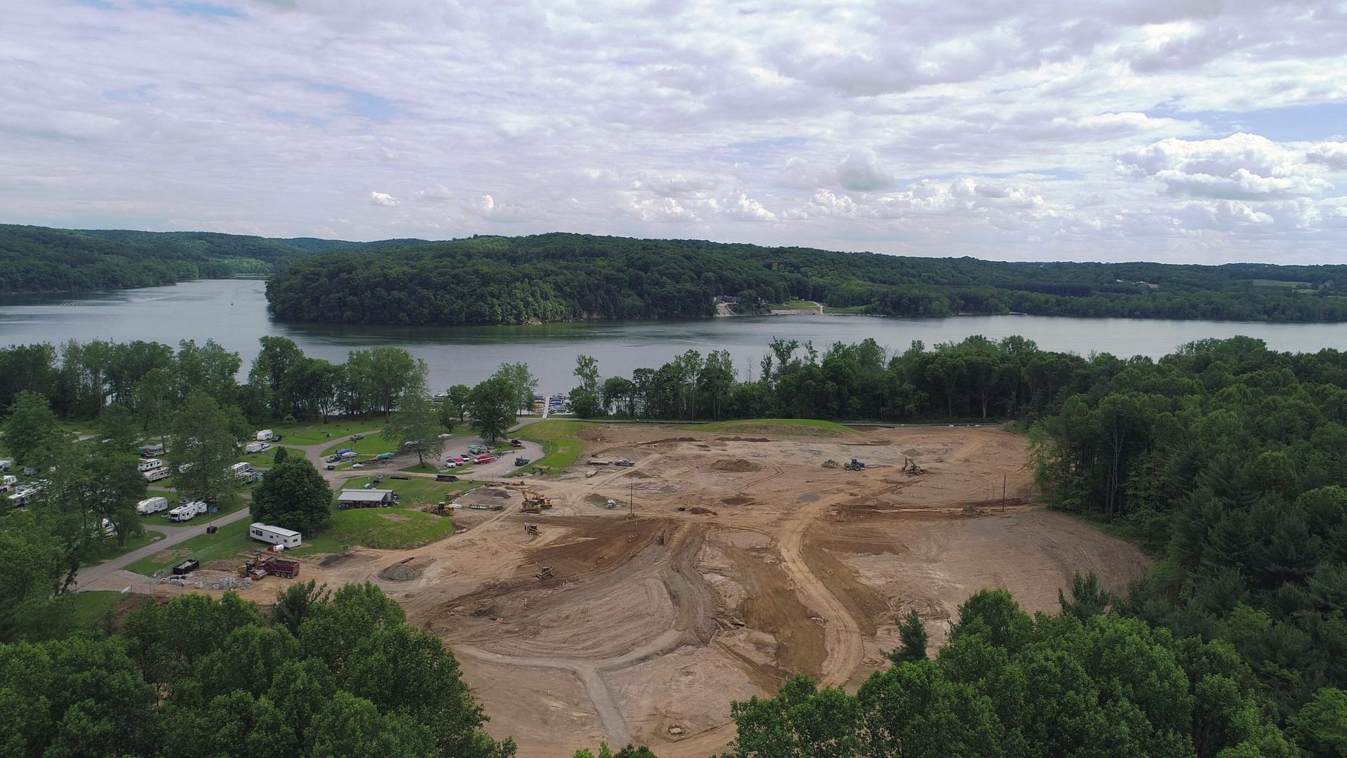 An aerial view of a construction site next to a lake surrounded by trees.
