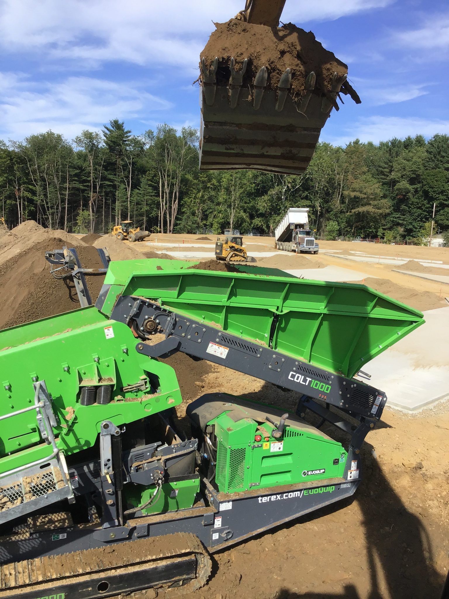 A green and black machine is loading dirt into a dump truck.