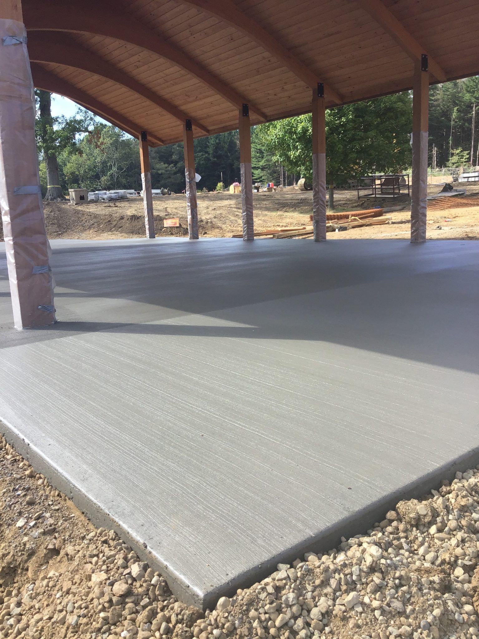 A concrete floor under a pavilion with a wooden roof.