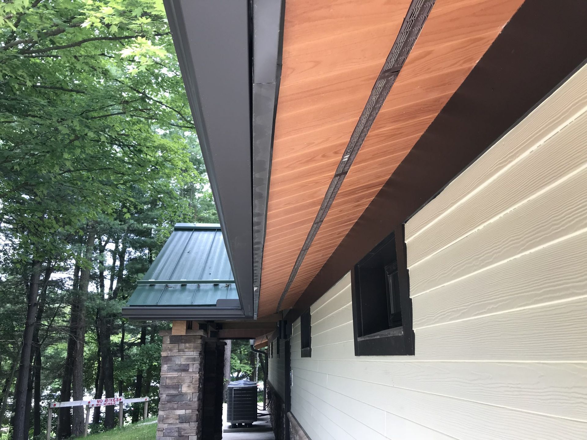 A house with a wooden roof and a green roof is surrounded by trees.