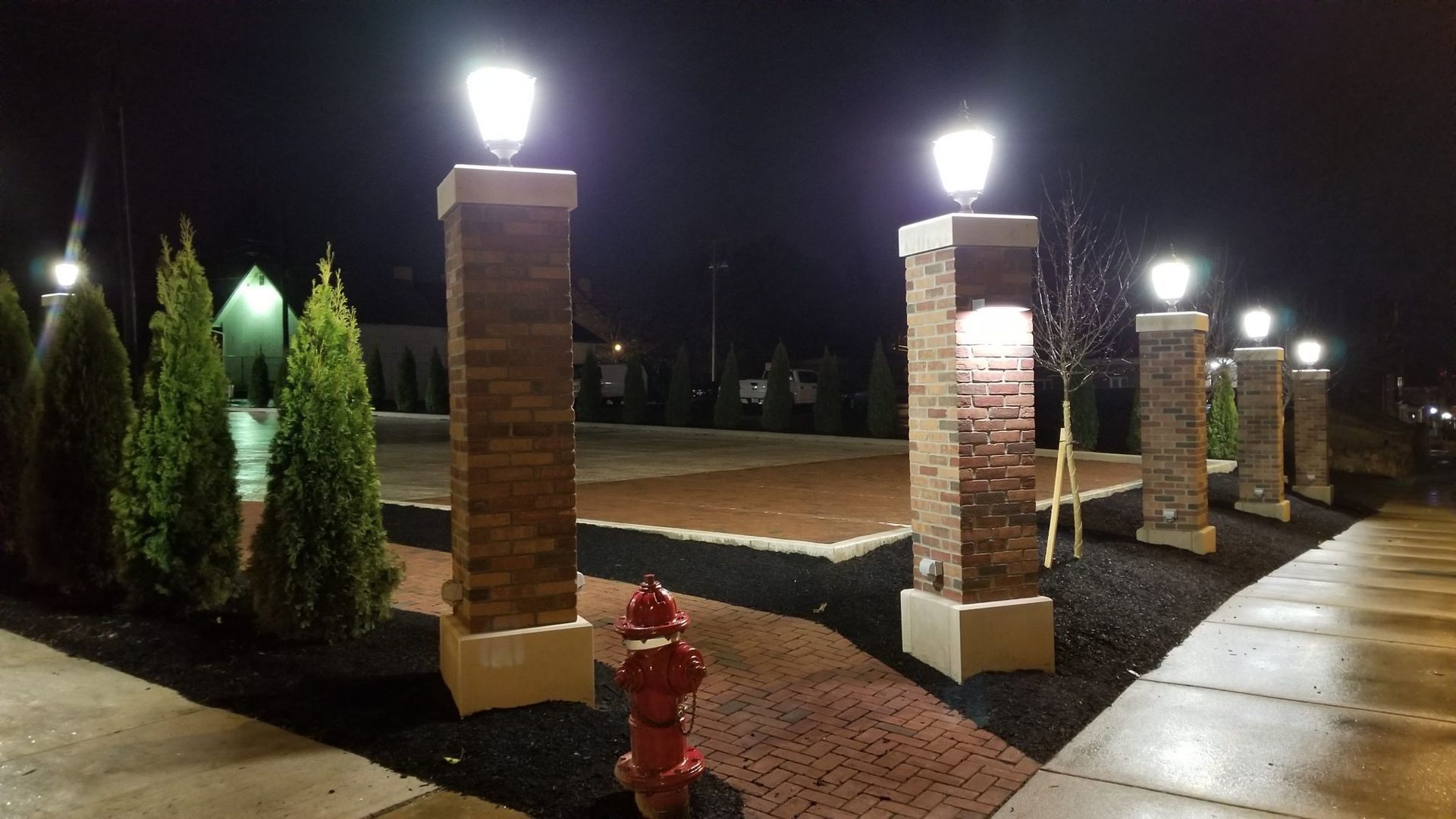 A fire hydrant sits next to a row of brick pillars at night.