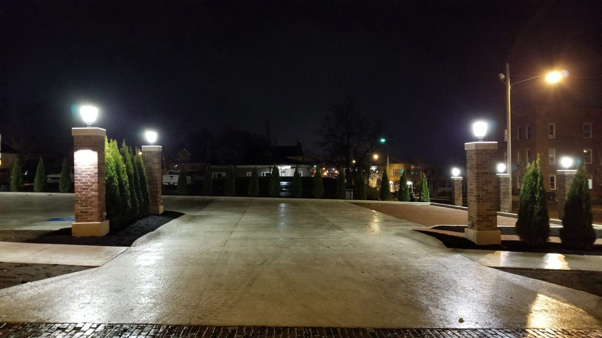 A driveway with pillars and lights at night.