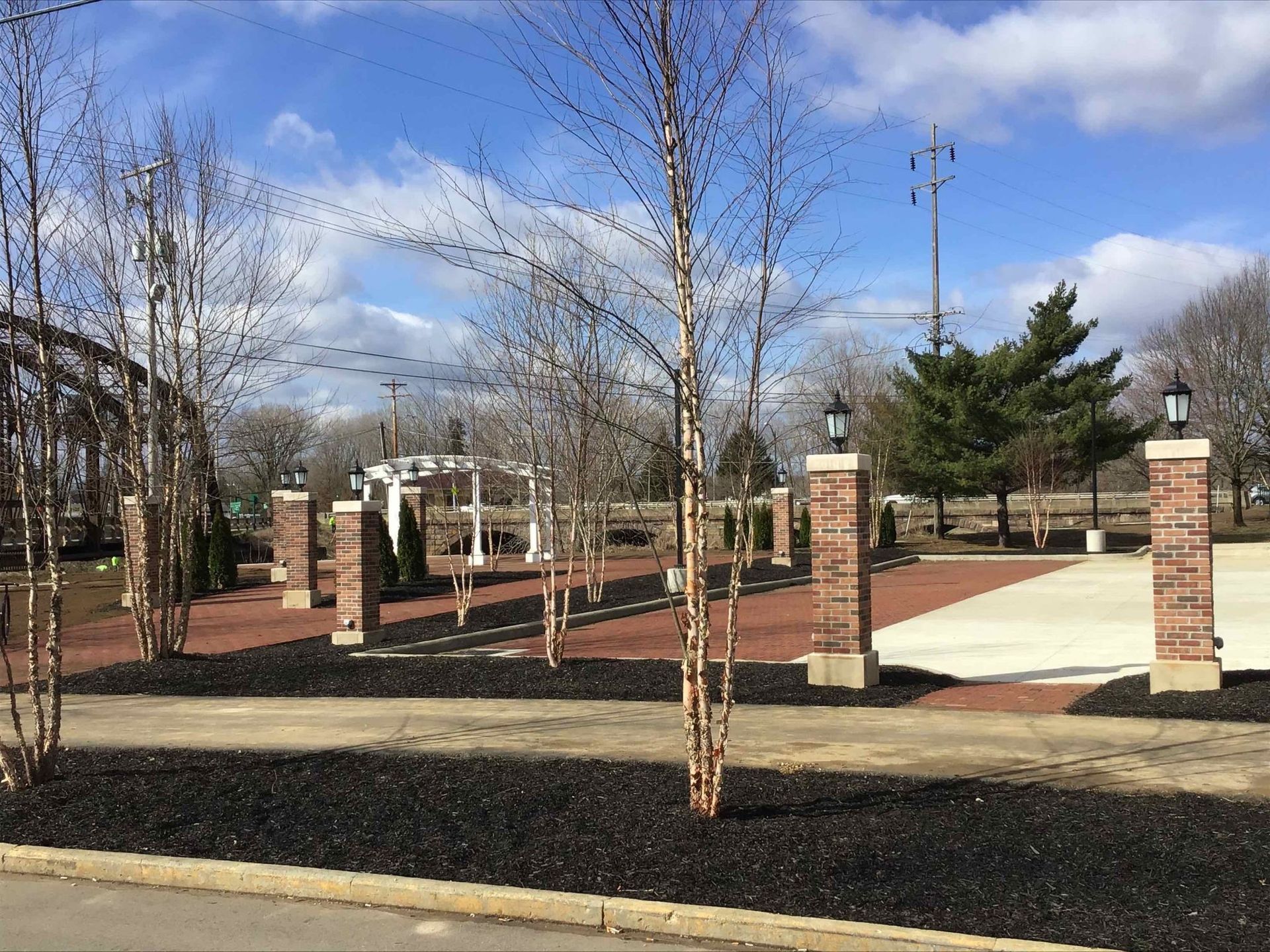 A park with trees and brick pillars on a sunny day.