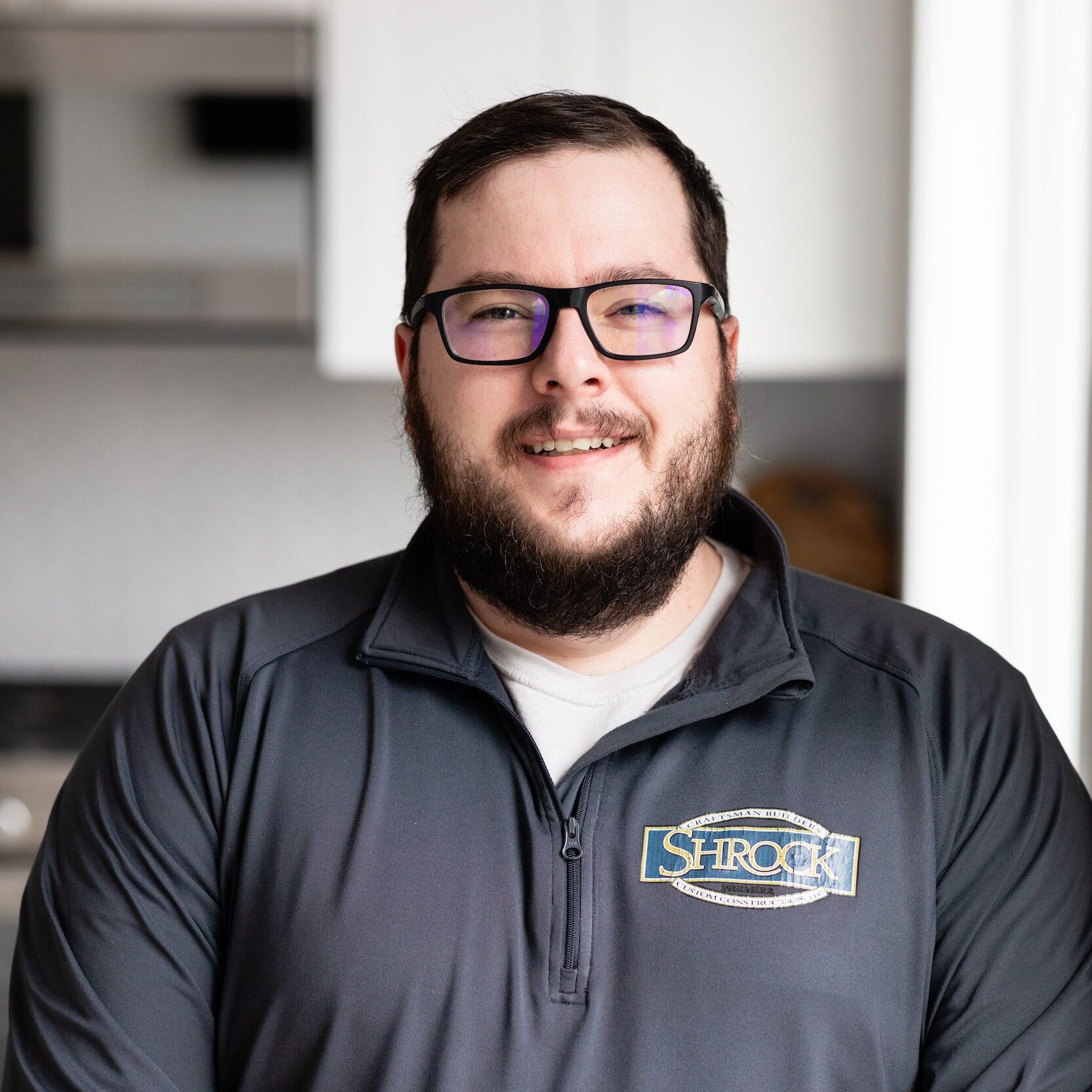 A man with a beard and glasses is wearing a black jacket.