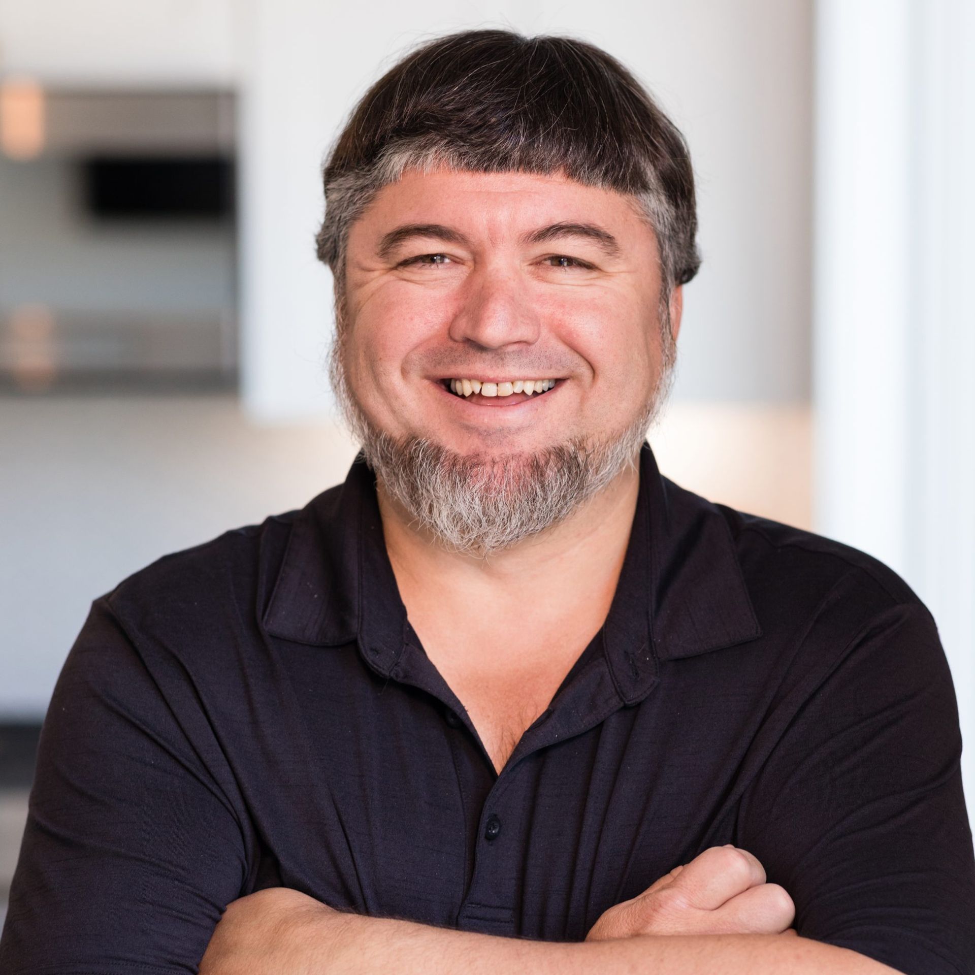 A man with a beard is smiling with his arms crossed