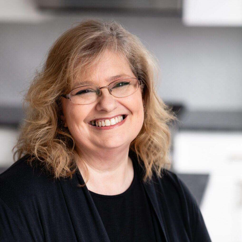 A woman wearing glasses and a black shirt is smiling for the camera.