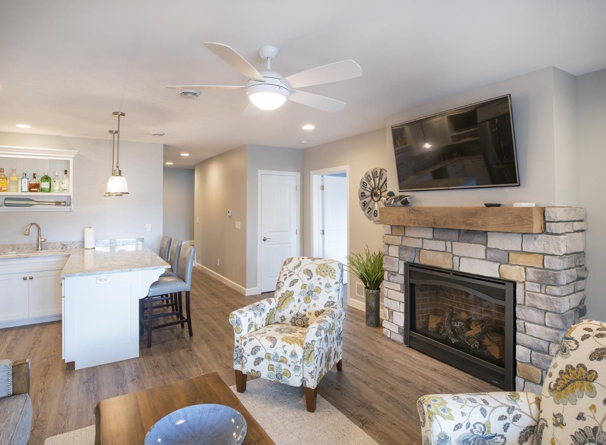 A living room with a fireplace , chairs , a television and a ceiling fan.