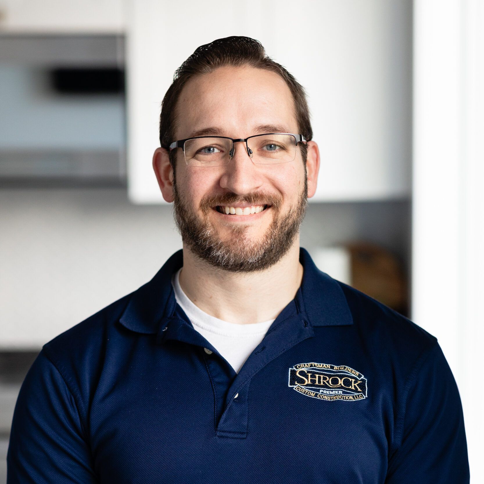 A man with a beard and glasses is wearing a blue shirt and smiling.