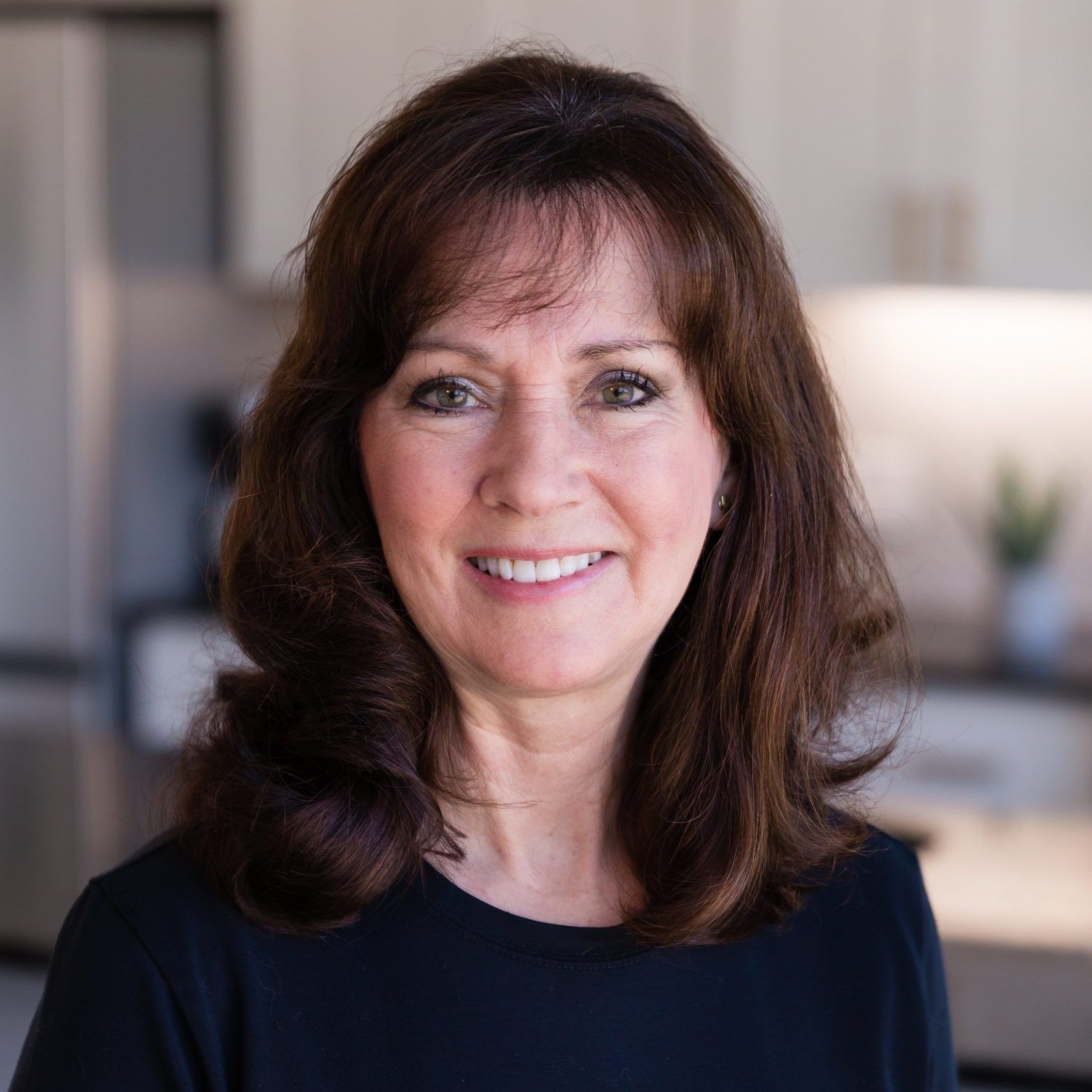 A woman in a black shirt is smiling for the camera in a kitchen.