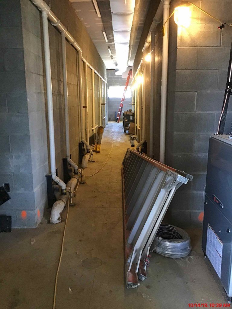 A long hallway with pipes and a ladder in a building under construction.
