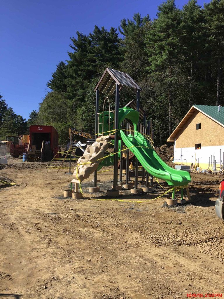 A green playground set is being built in a dirt field.