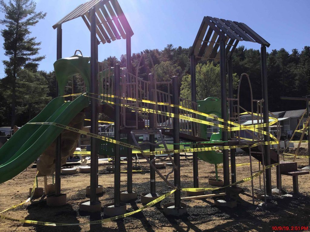 A playground with a green slide and yellow tape around it.