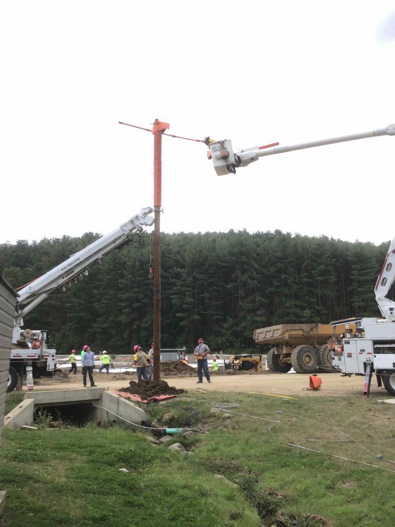 A crane is lifting a pole in a field.