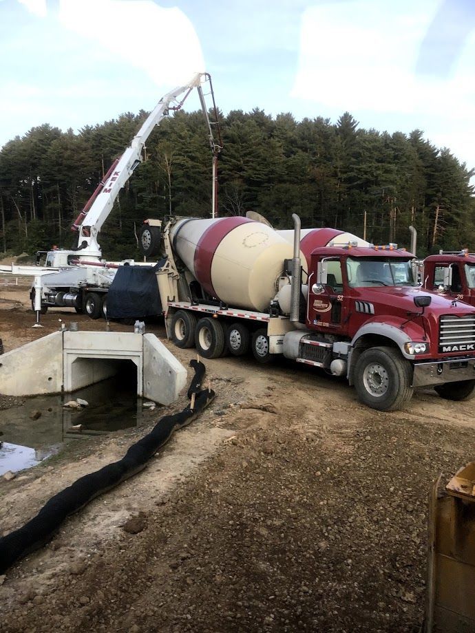 A concrete mixer truck is driving down a dirt road.