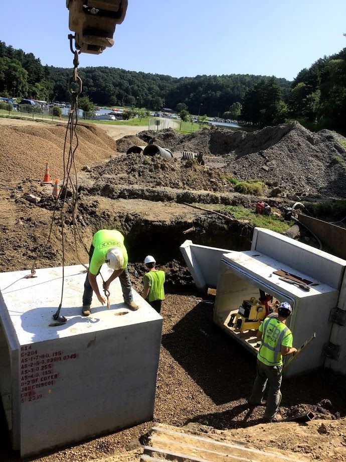A group of construction workers are working on a large concrete block being. lifted by a crane.