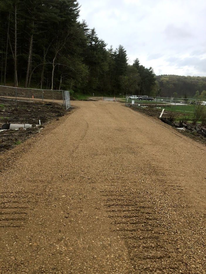 A gravel road going through a forest with trees on both sides.