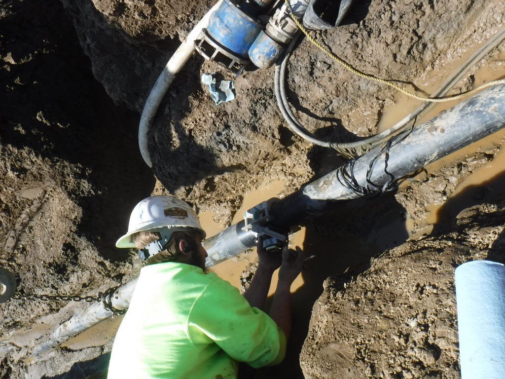A man wearing a hard hat is working on a pipe in the dirt