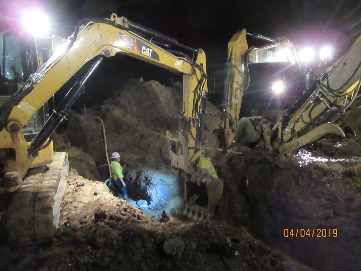 A man is standing next to a large yellow excavator at night.