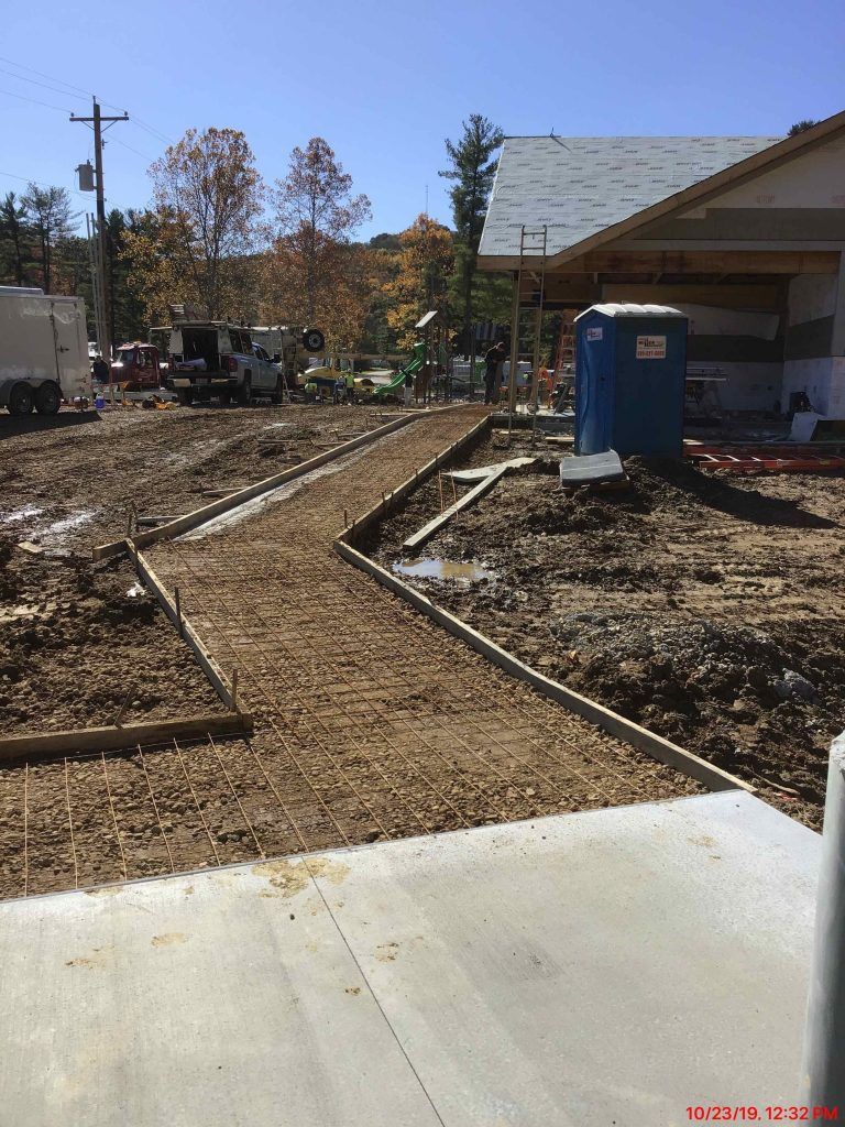 A blue portable toilet is sitting in the dirt in front of a building under construction.