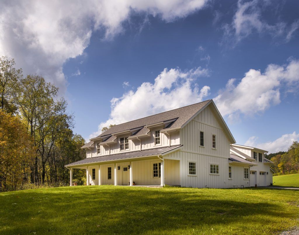 A large white house with a porch and trees in the background.