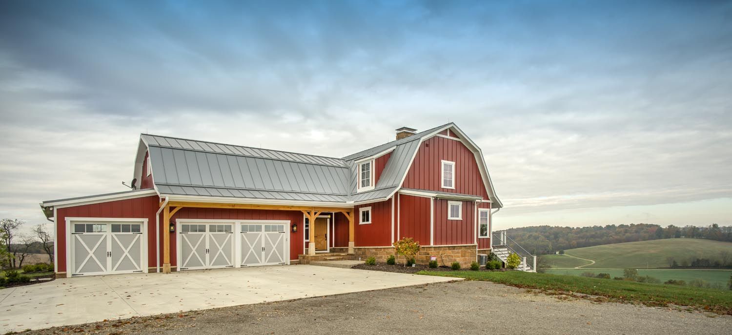 A large red barn is sitting on top of a  hill with beautiful scenery in the background.