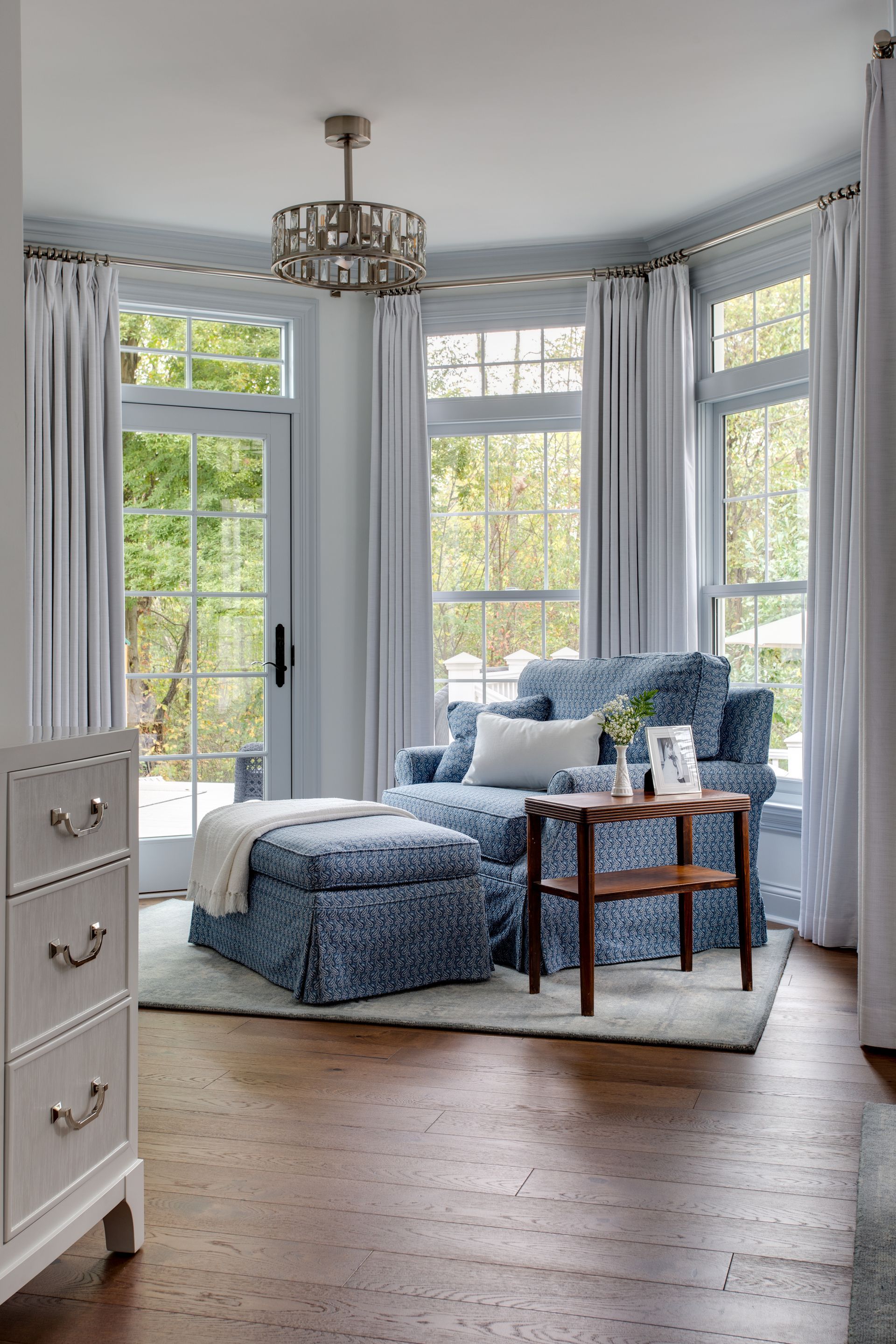 A living room with a blue chair, ottoman, table and dresser.
