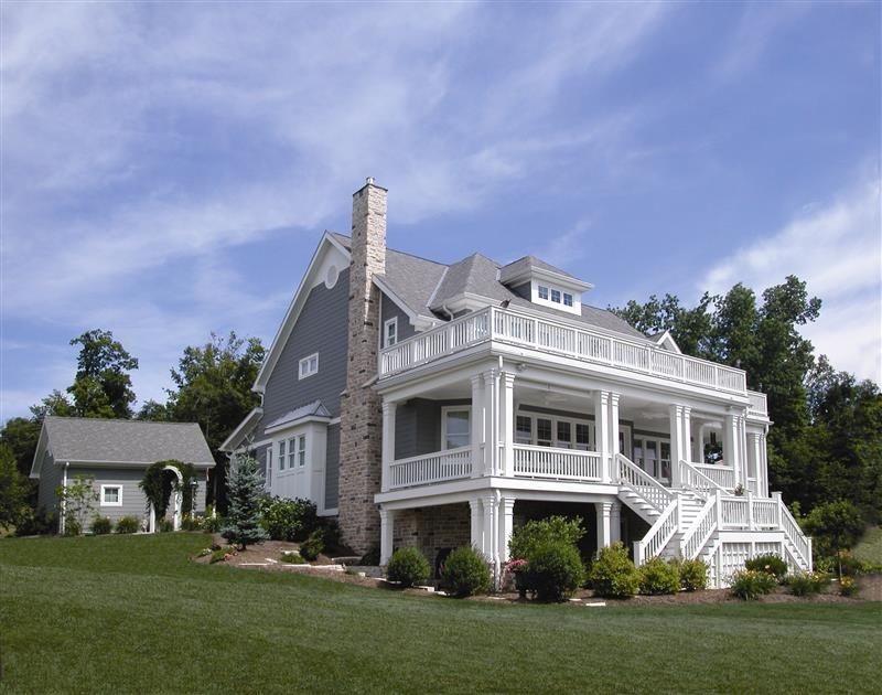 Large gray Victorian house with white trim and wraparound porch on a green lawn under a blue sky.