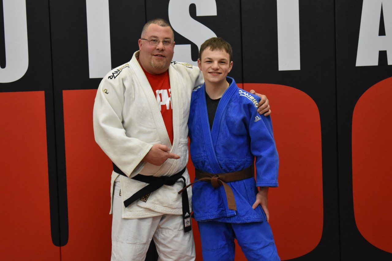 A man and a boy are posing for a picture in front of a judo wall
