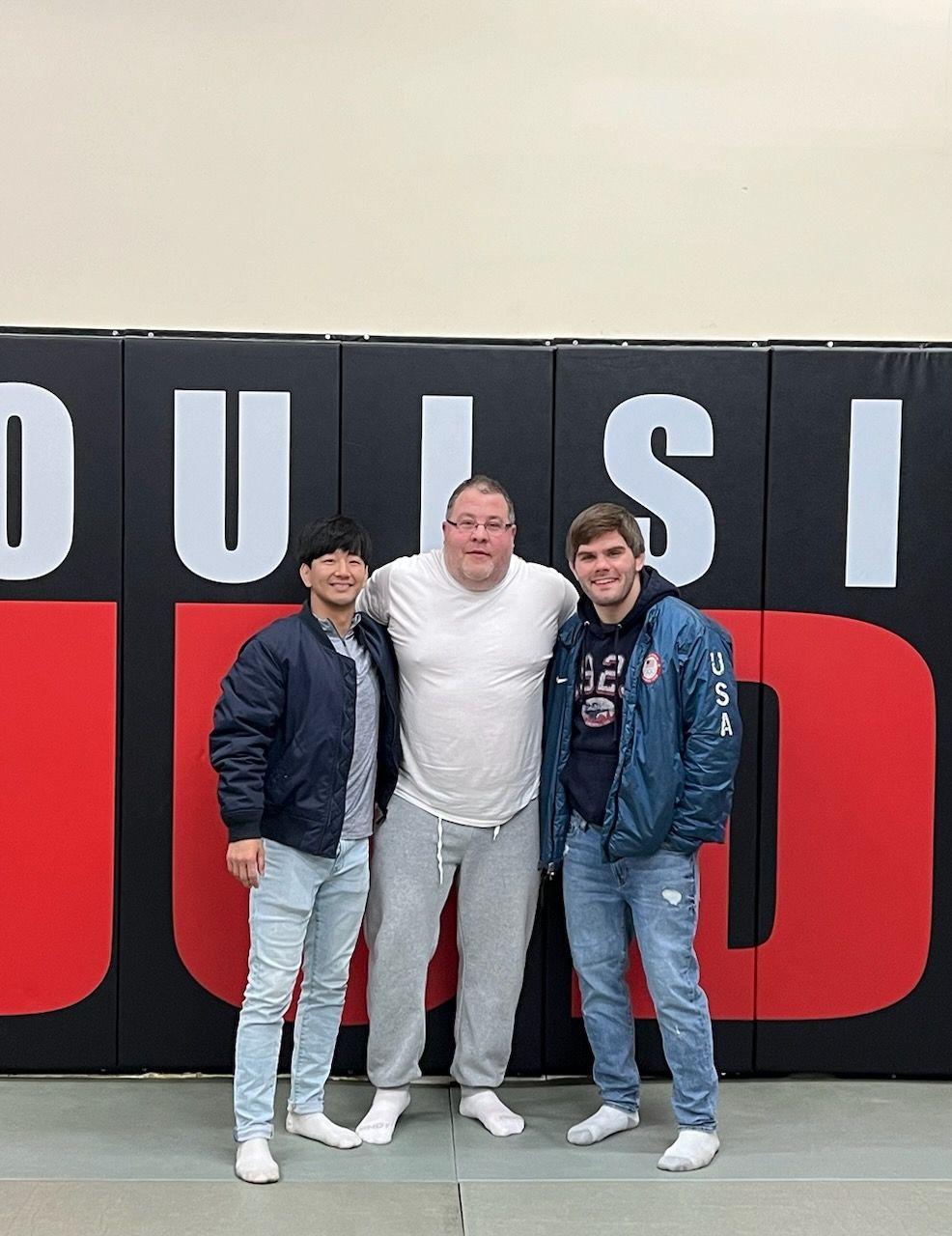 Three men are posing for a picture in front of a wall with the word dulsa on it.