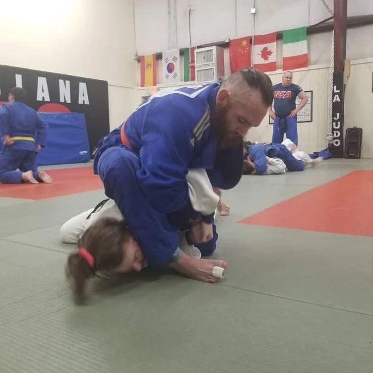 A group of people are practicing judo in a gym with a sign that says lana