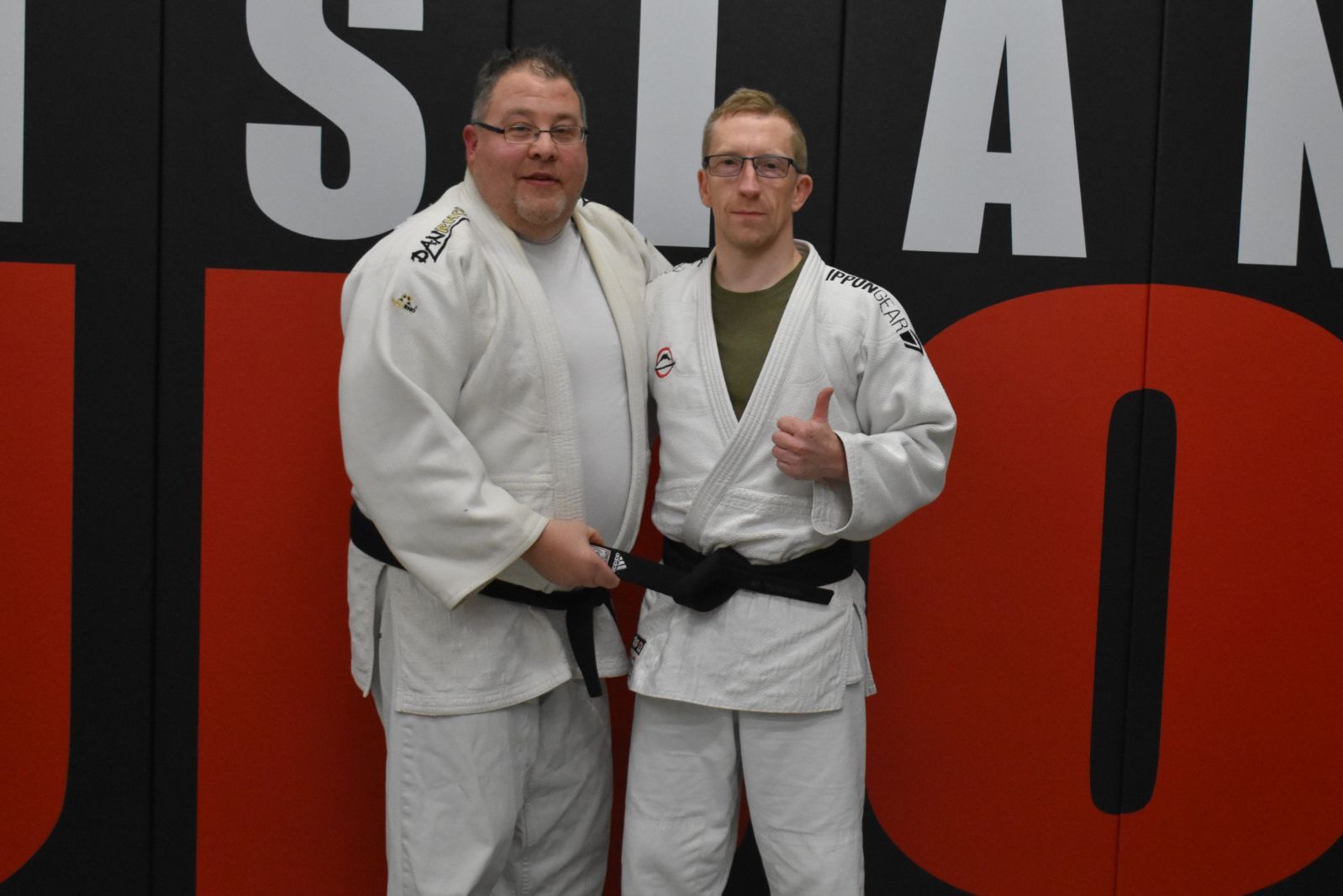 Two men are posing for a picture in front of a judo wall
