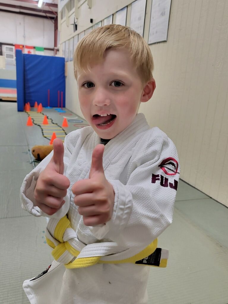 A young boy in a karate uniform is giving a thumbs up.