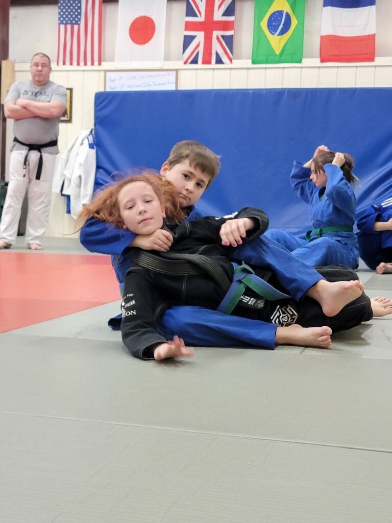 A boy and a girl are wrestling on a mat in a gym.