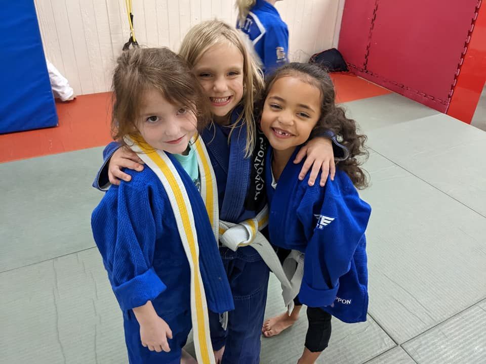 Three young girls wearing blue and yellow karate uniforms are posing for a picture.