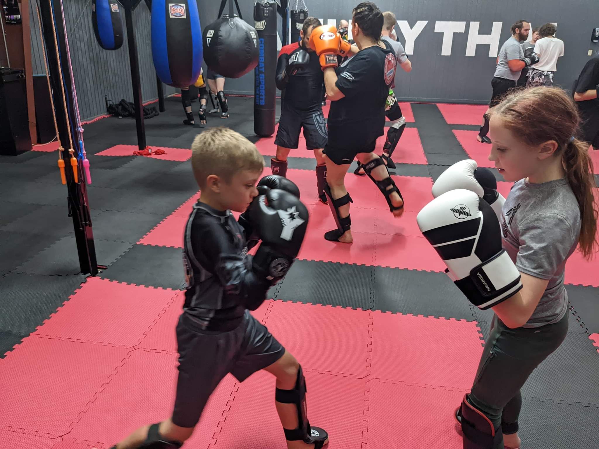 A boy and a girl are boxing in a gym.