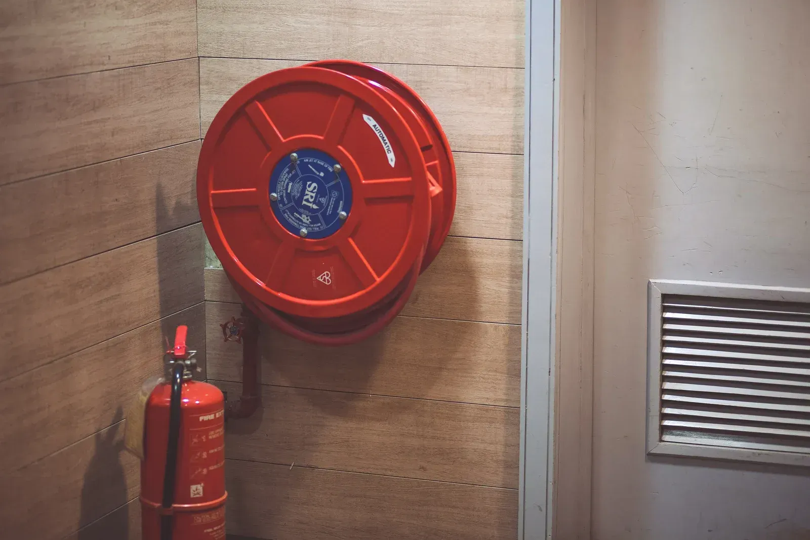 Red fire hose reel and extinguisher on a wooden wall next to a door.