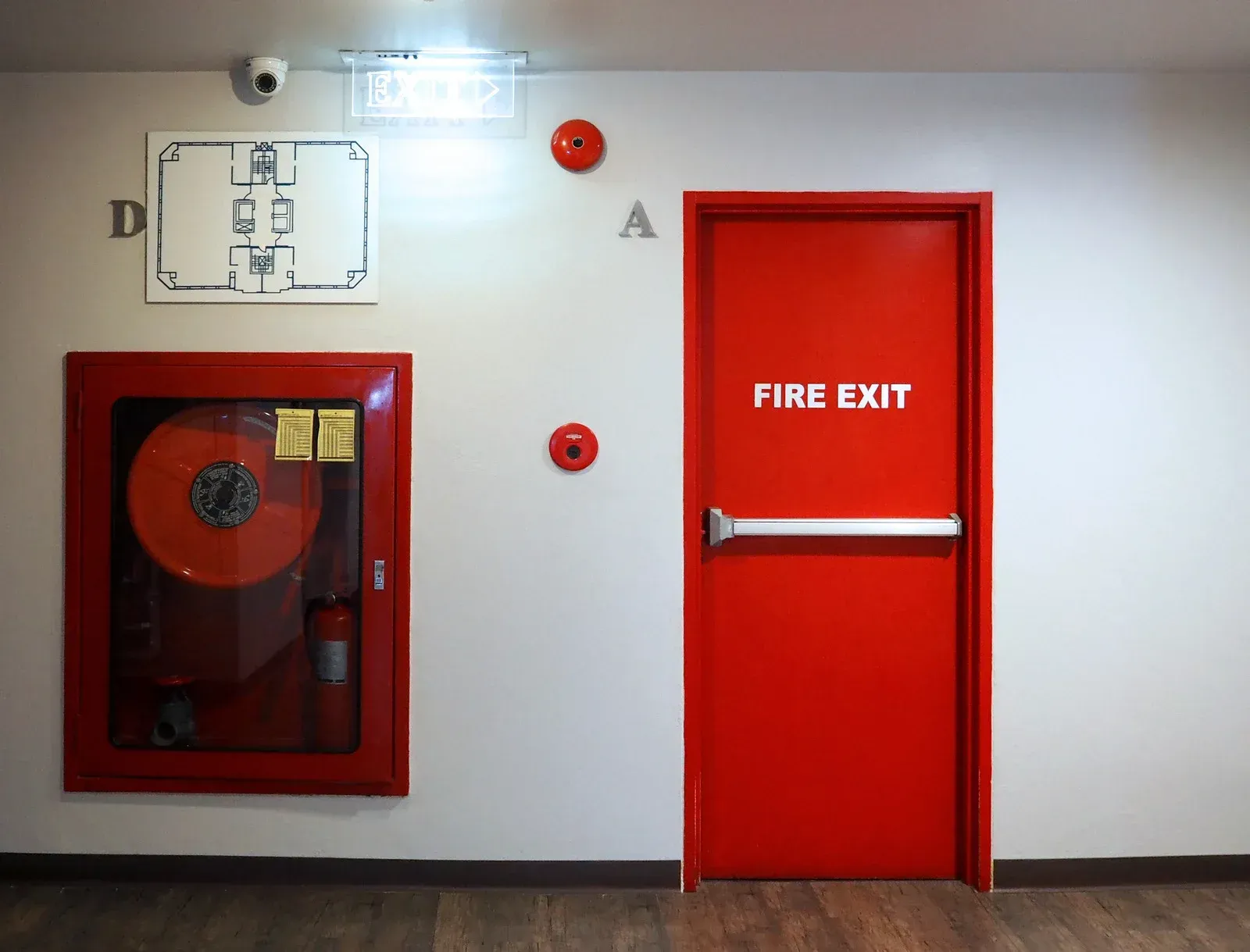 Red fire exit door, fire hose, and fire alarm equipment in hallway.