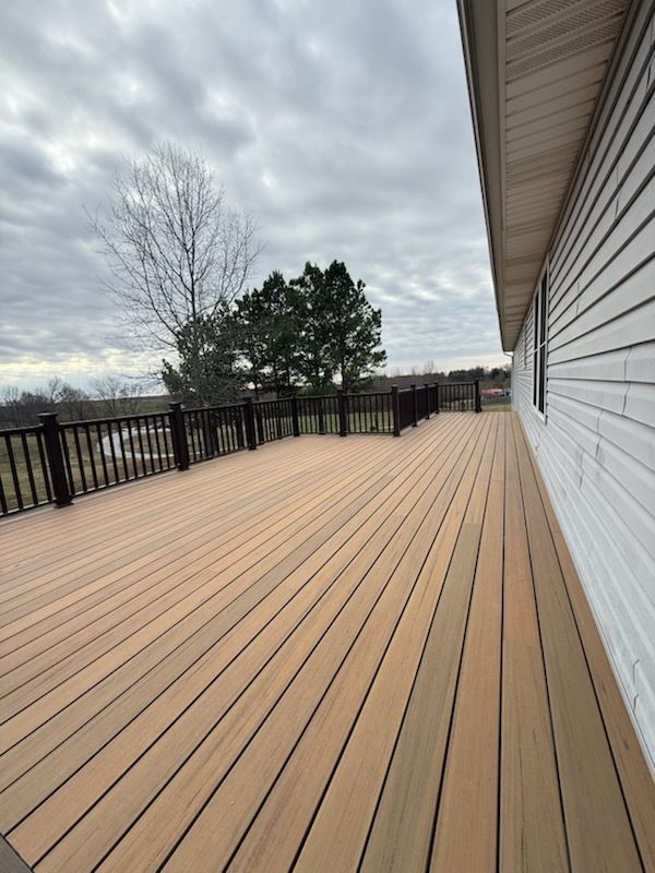 Empty wooden deck beside white house under cloudy sky, with black railing and trees in the distance