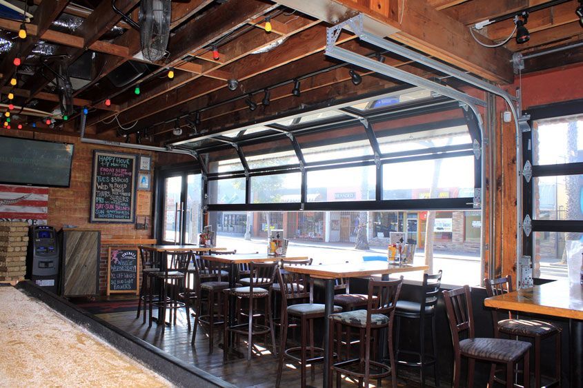 A restaurant with tables and chairs and a large garage door.
