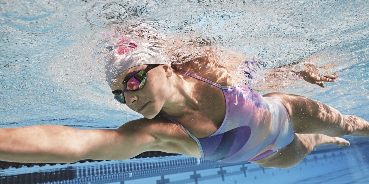 A woman is swimming in a pool wearing a hat and goggles.