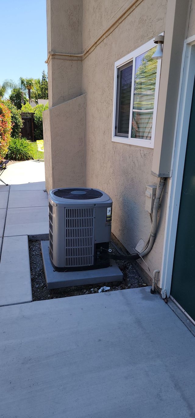 Outdoor HVAC unit beside a stucco wall and window on a concrete patio walkway