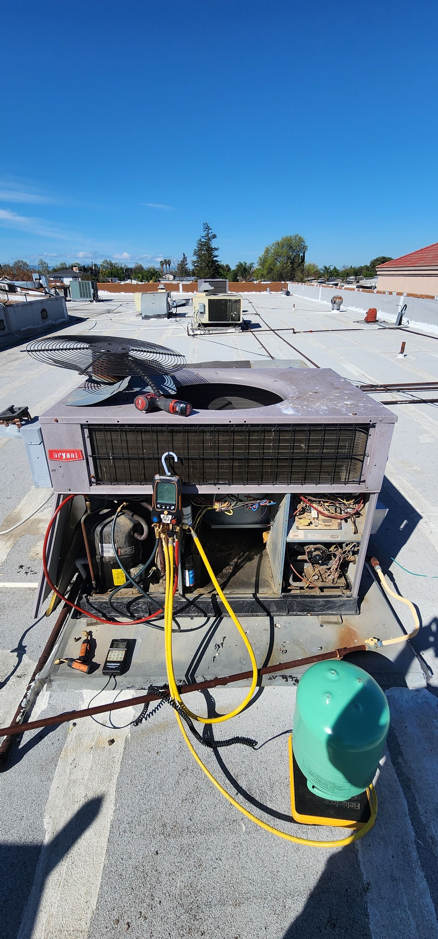 Rooftop HVAC units and hoses under a bright blue sky, with workers and tools visible in the foreground