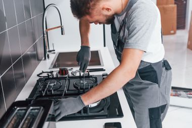 Technician in gray uniform cleaning a black gas stovetop in a modern kitchen